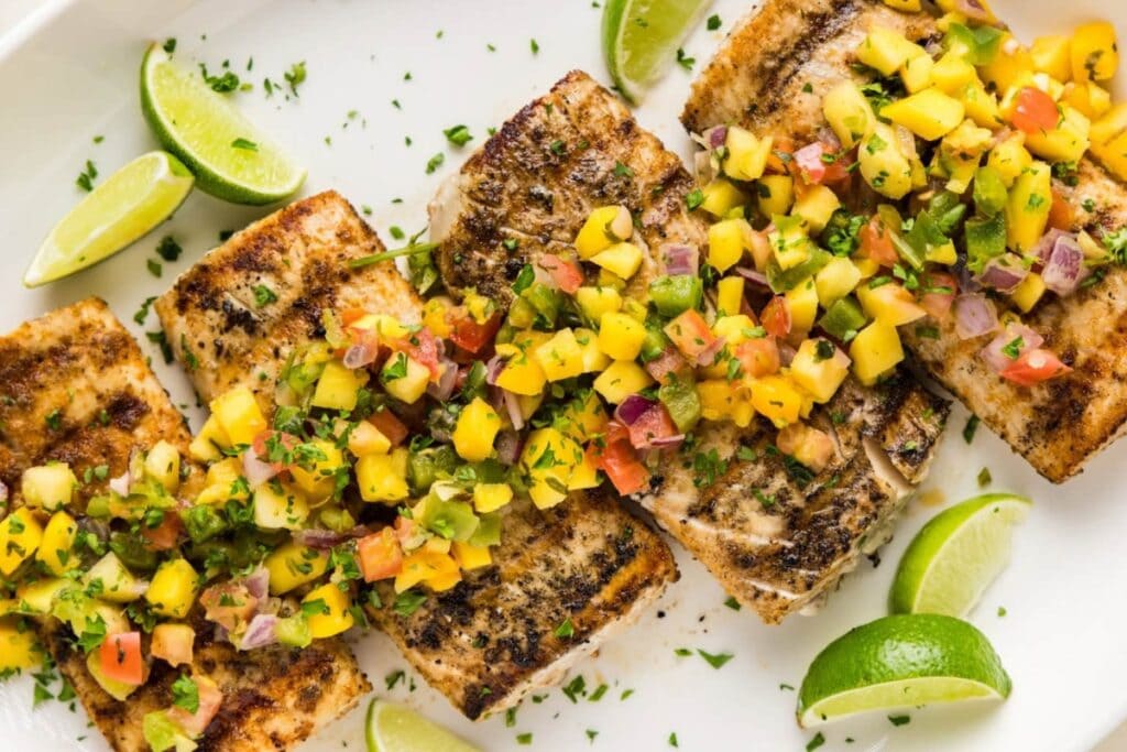 Grilled mahi mahi on a white plate, garnished with herbs and lemon.