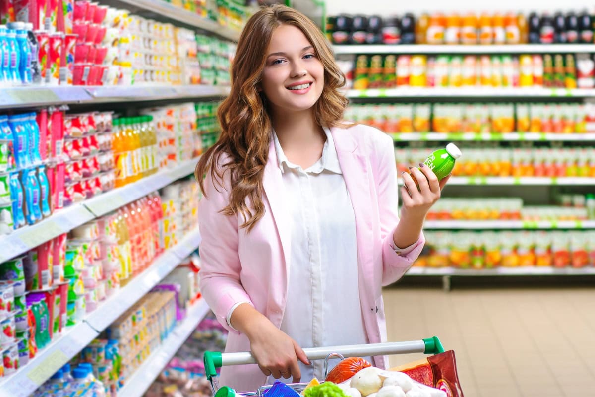 Female shopper with a bottle and shopping cart in a supermarket.