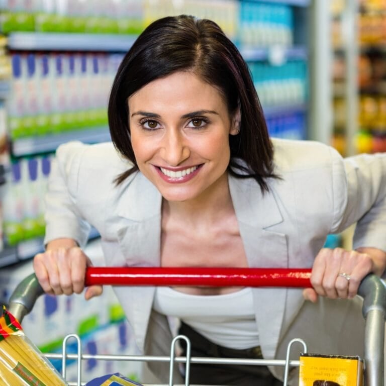 Smiling woman pushing a cart down a grocery store aisle.