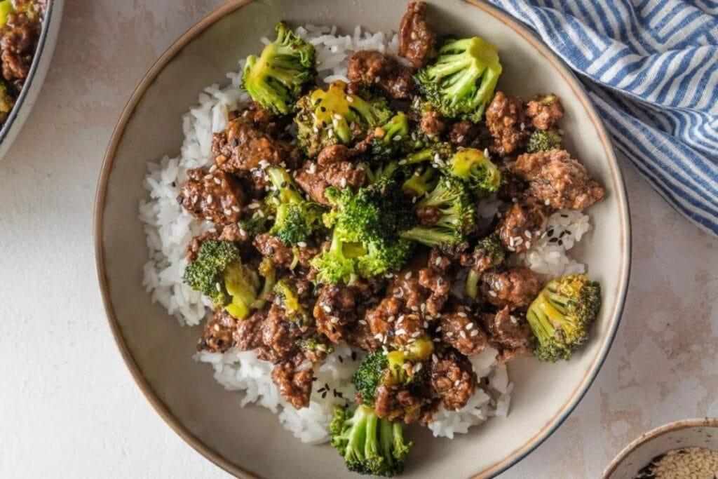 Ground beef and broccoli served with rice on a white plate.