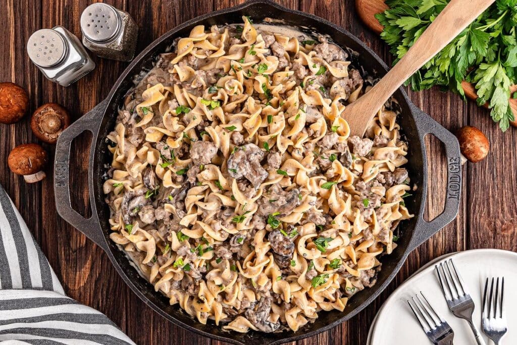 Ground beef stroganoff in a black skillet with a wooden serving spoon.