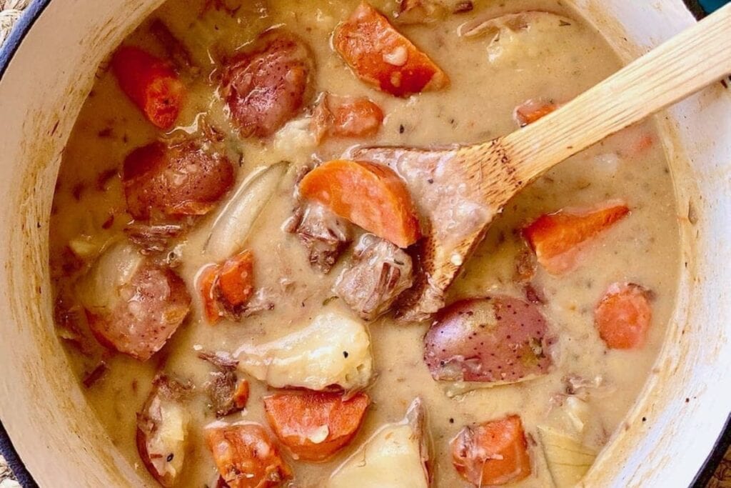 Hearty beef stew in a Dutch oven with a wooden spoon.