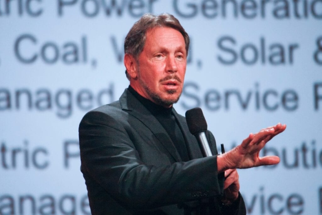 Larry Ellison in a black suit speaking on stage.