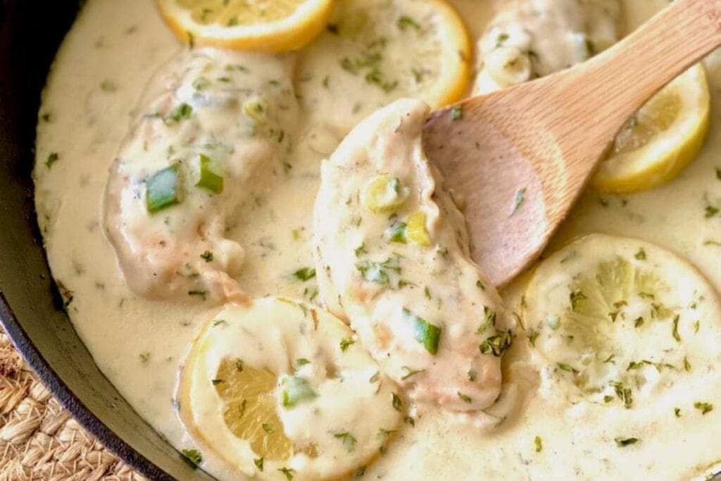 Lemon butter chicken in a skillet with a wooden spoon.