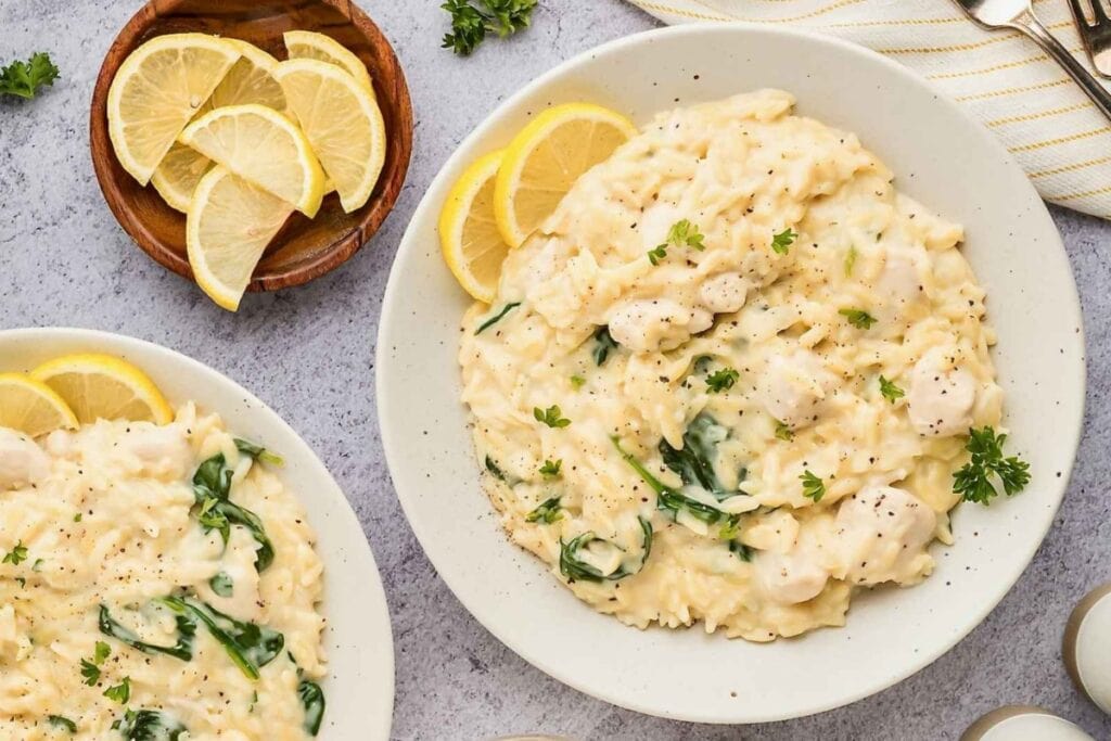 Lemon chicken orzo pasta on a white plate with a slice of lemon.