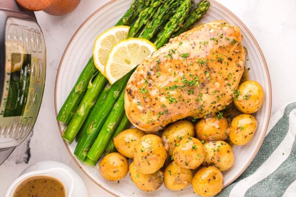Lemon garlic chicken and potatoes with asparagus on a white plate.
