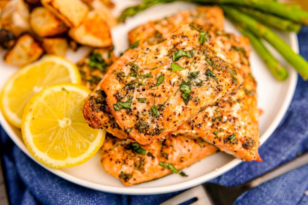 Lemon garlic salmon fillet served on a white plate, garnished with lemon slices and herbs.