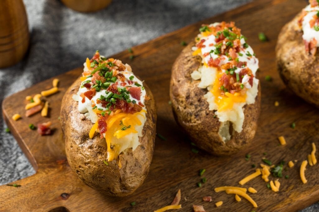 Loaded baked potatoes on a wooden board.