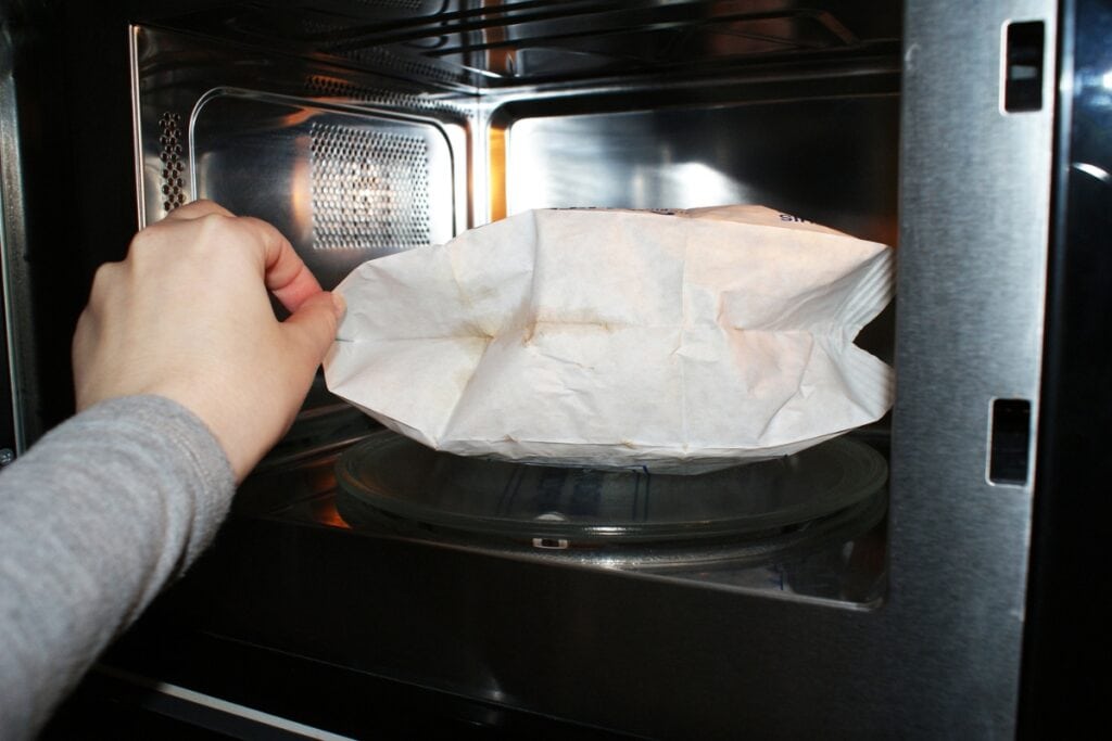 Woman placing a popcorn bag into a microwave.