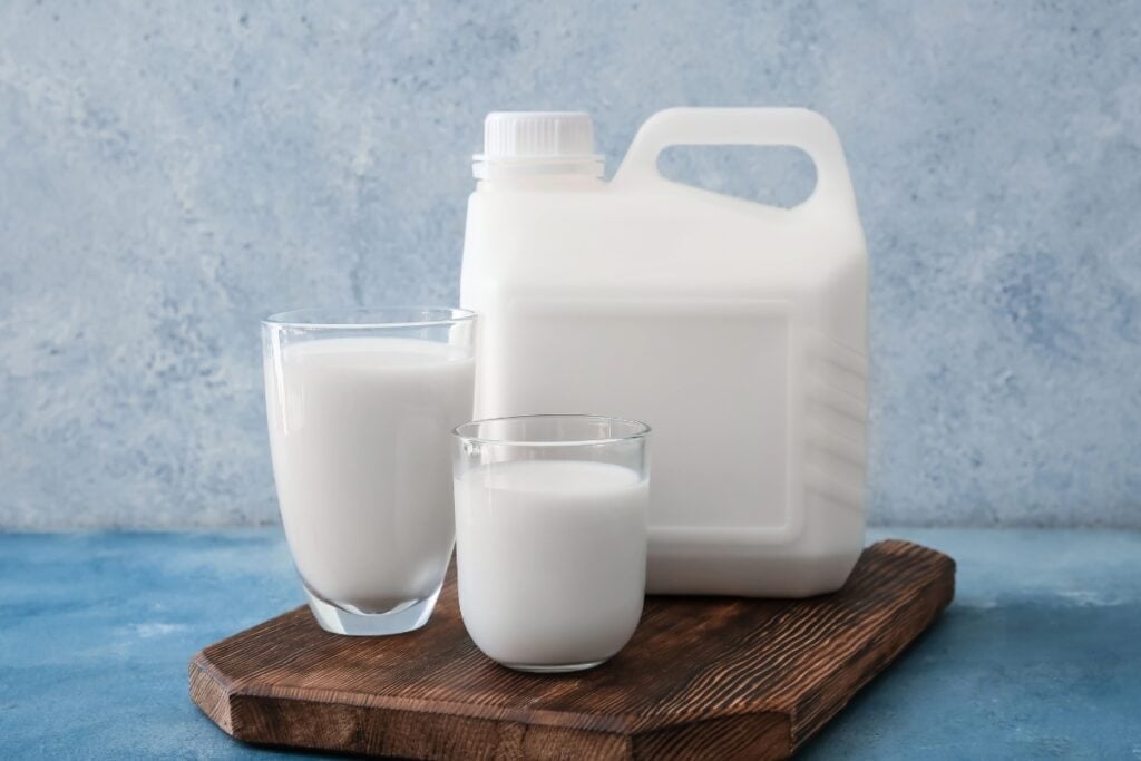 Gallon and two glasses of milk on a wooden board.