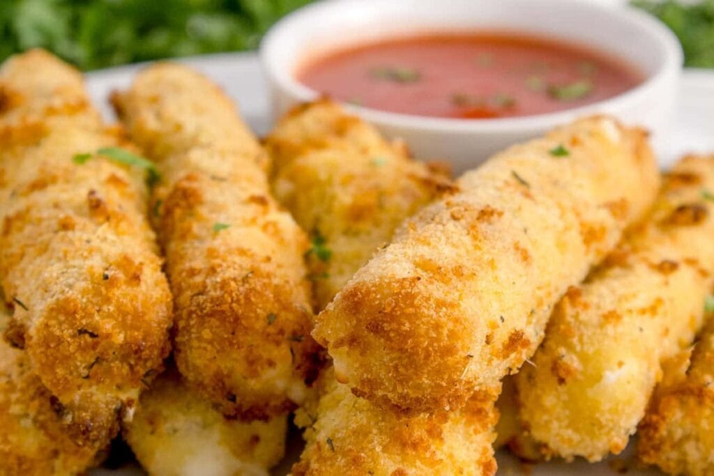 Mozzarella sticks on a white plate with dipping sauce in a small white bowl.