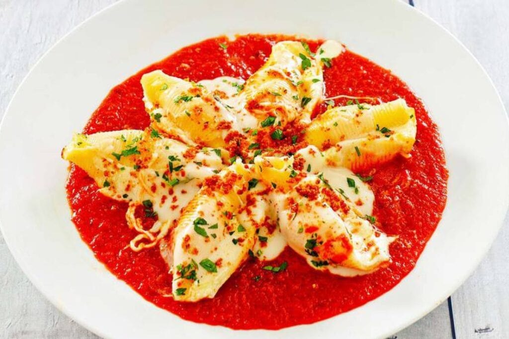 Olive Garden cheese stuffed shells on a white plate, served over marinara sauce.