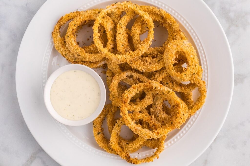 Onion rings on a plate with dipping sauce.