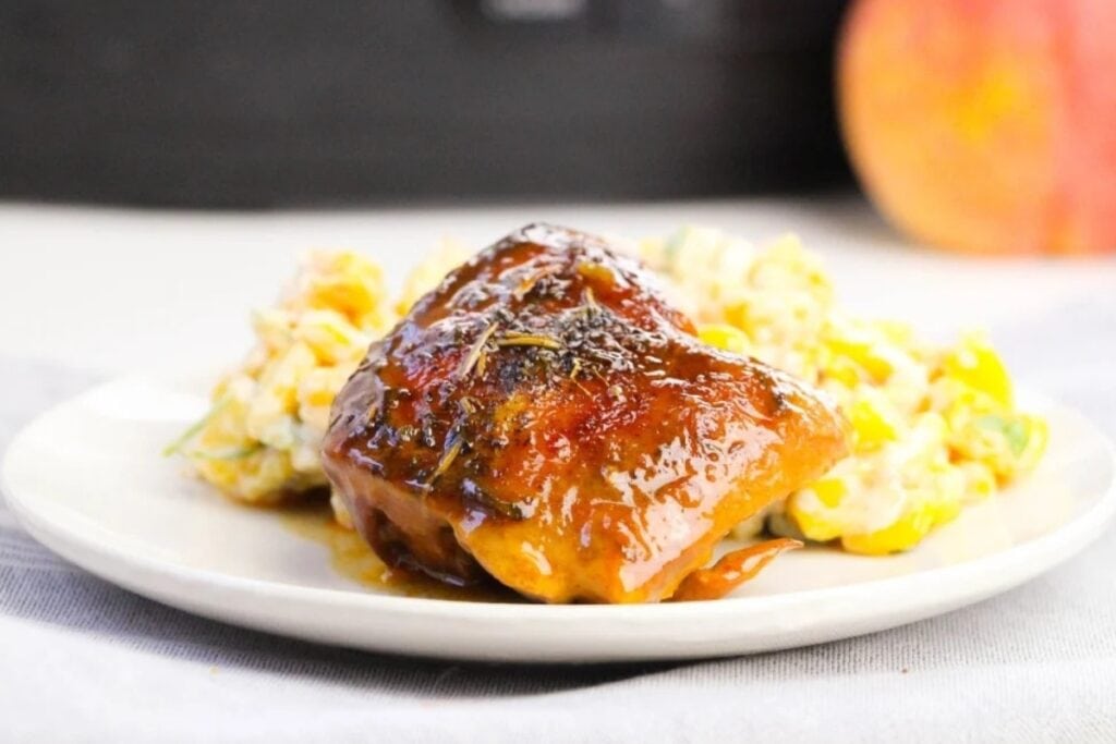 Peach BBQ chicken thighs served on a white plate.