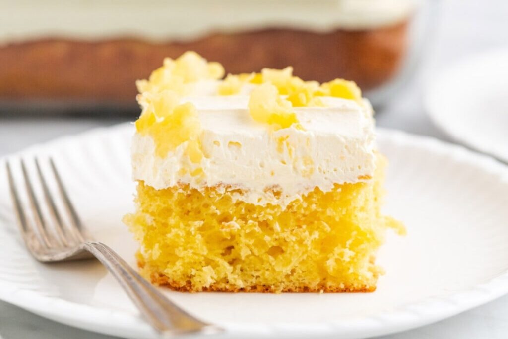 Pineapple Sunshine Cake on a white dessert plate with a fork on the side.