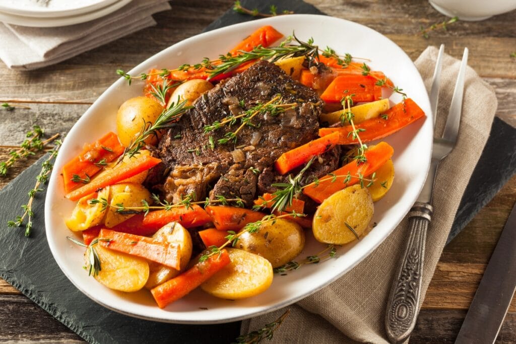 Pot roast on a white plate with vegetables.