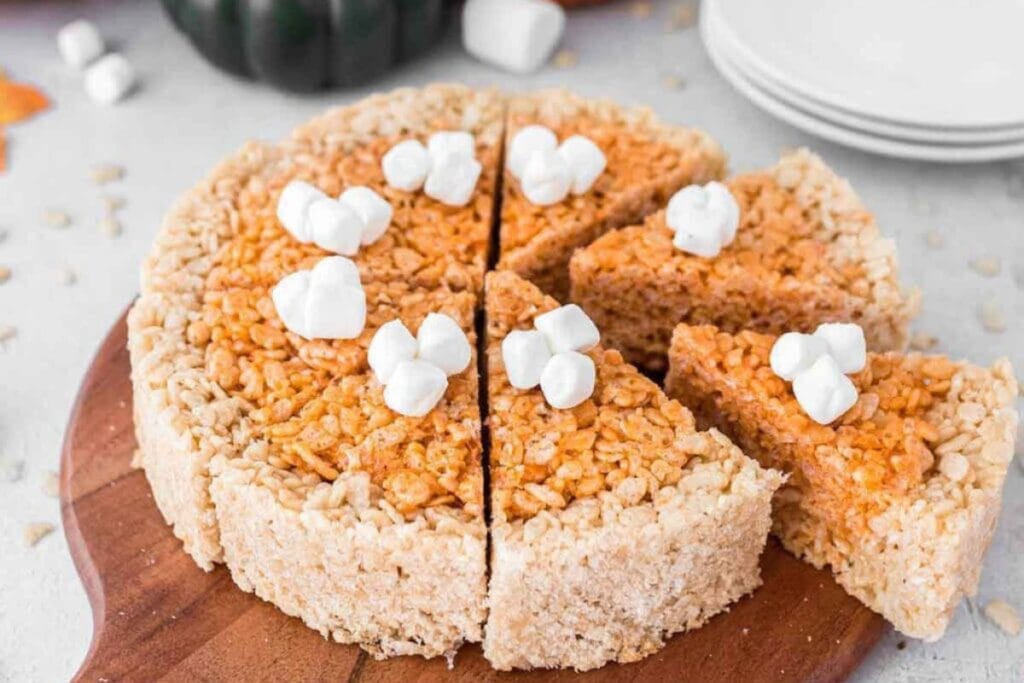 Whole pumpkin pie Rice Krispie treat with slices on a wooden board.