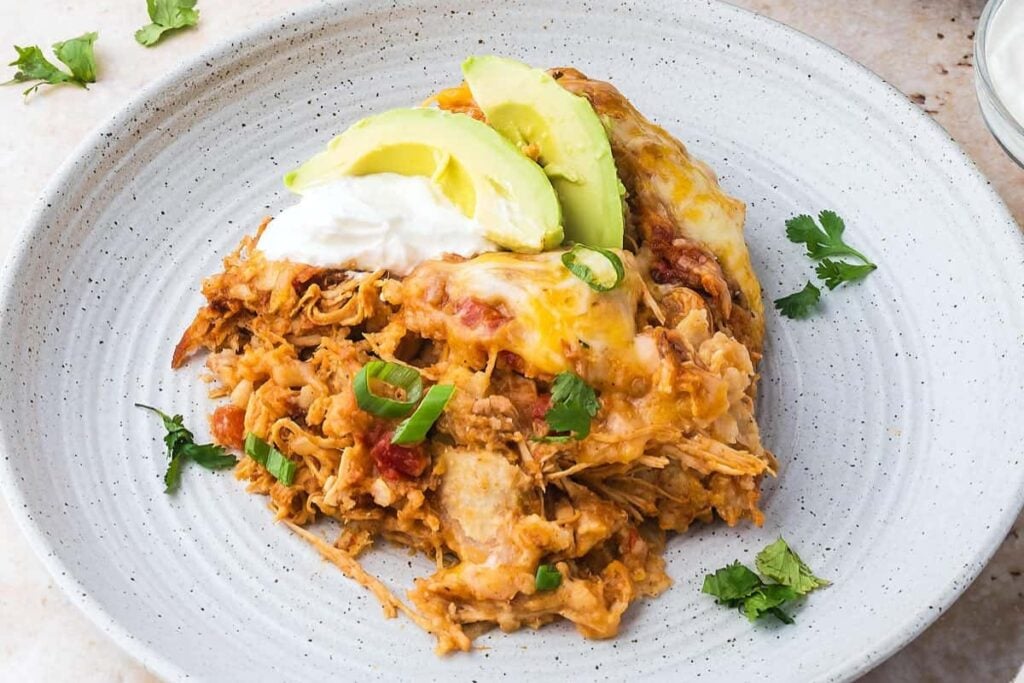 Chicken enchilada casserole scooped from slow cooker with wooden spoon.
