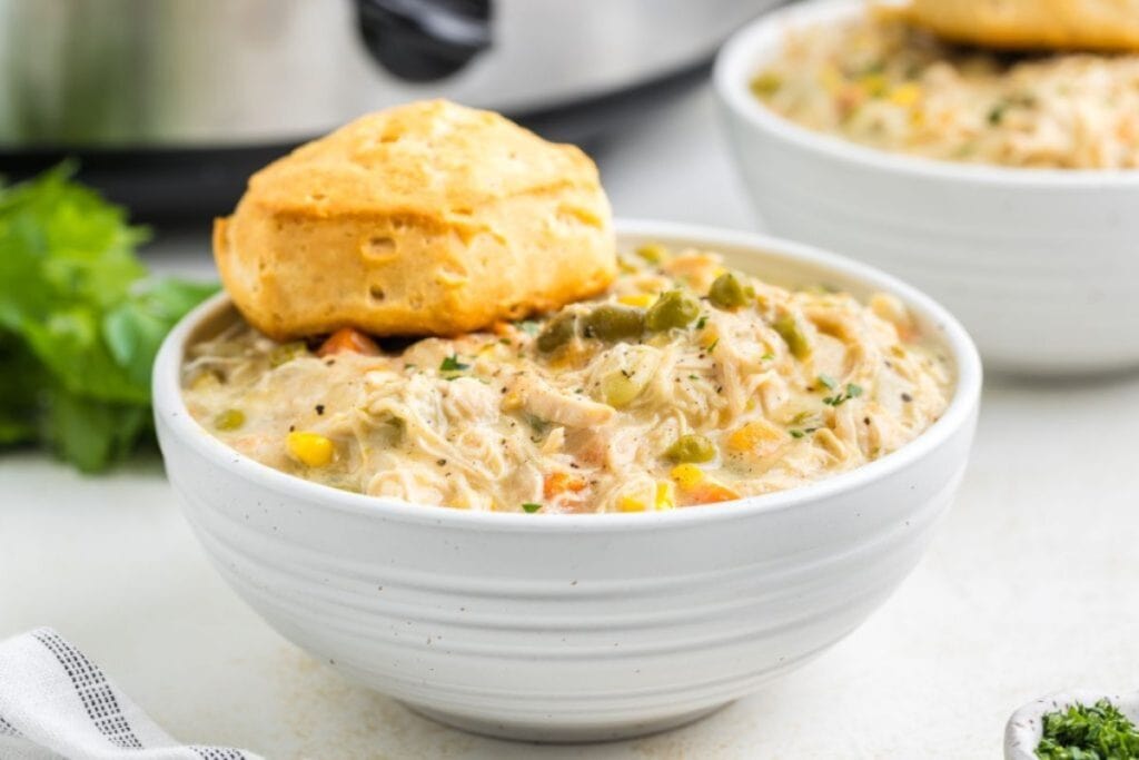 Slow cooker chicken pot pie in a white bowl topped with a biscuit.