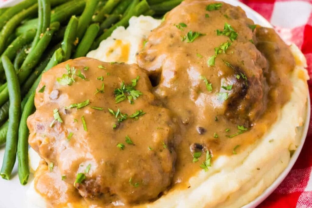 Slow cooker Salisbury steak served with green beans and rice on a plate.