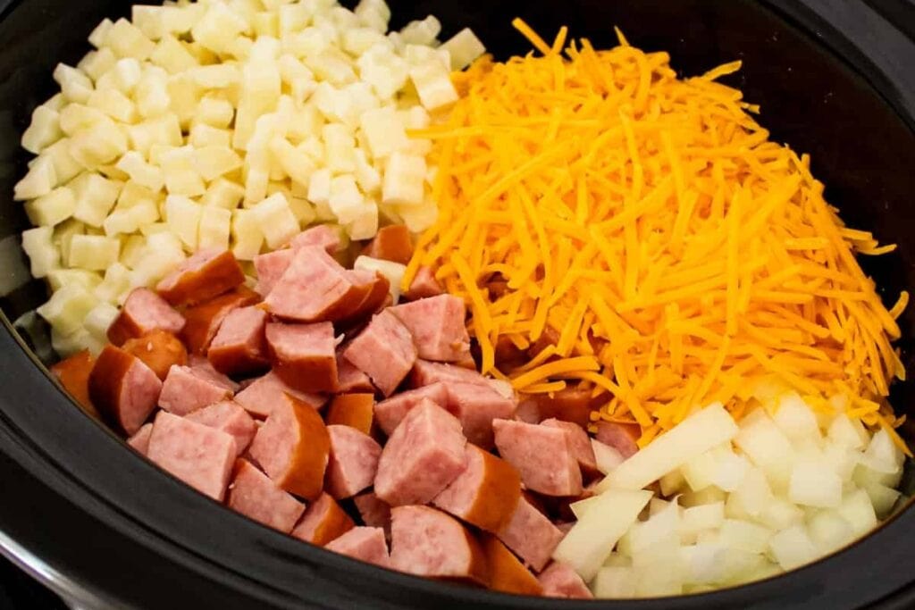Sausage and potato casserole ingredients in a slow cooker.