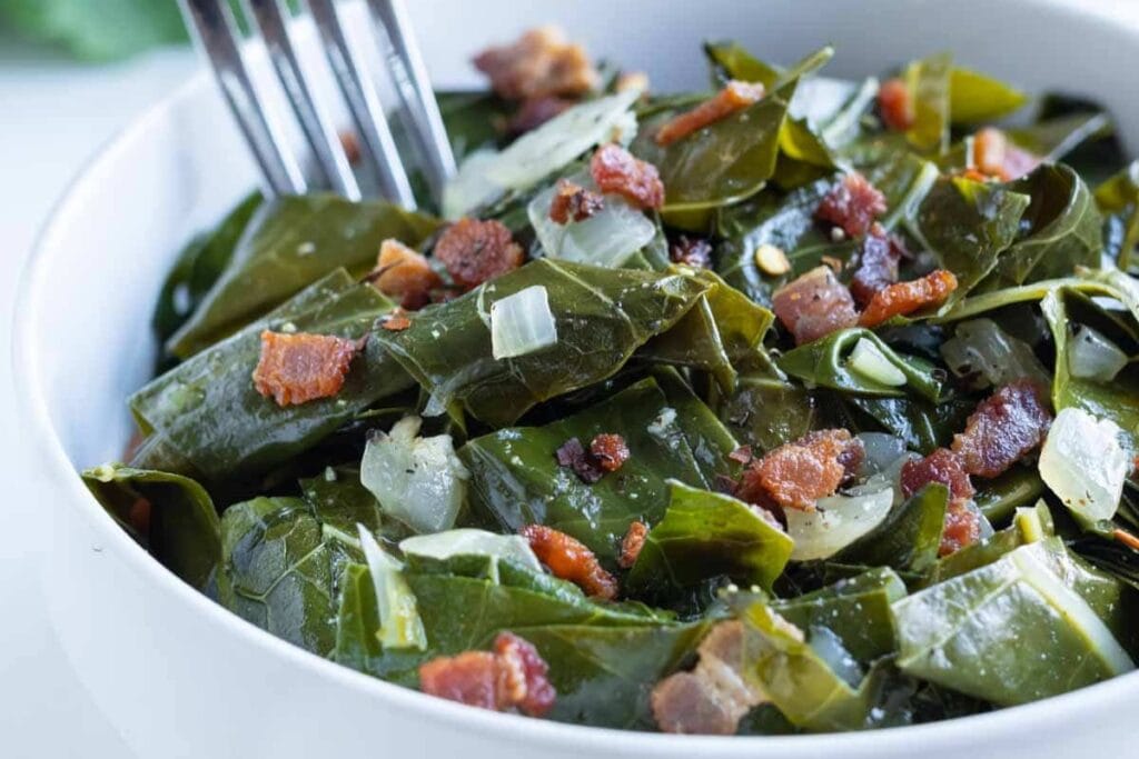 Southern collard greens with bacon and onions in a white bowl with a fork.