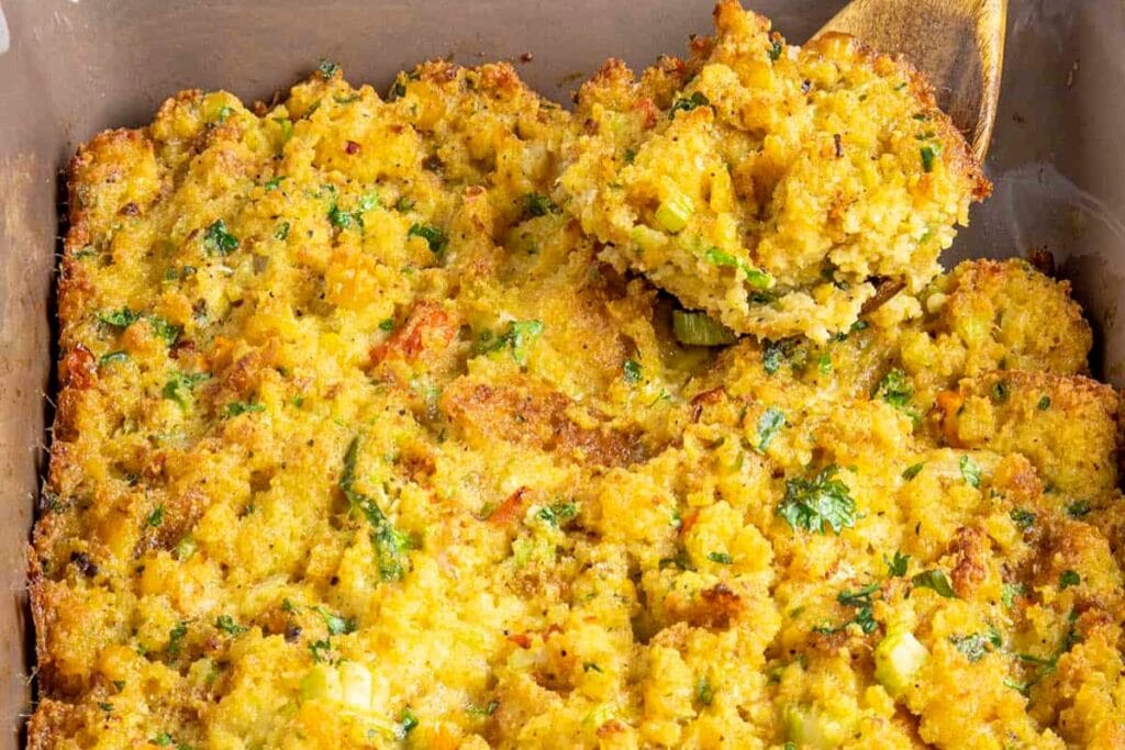 Southern cornbread dressing scooped with a wooden spoon in a rectangular dish.