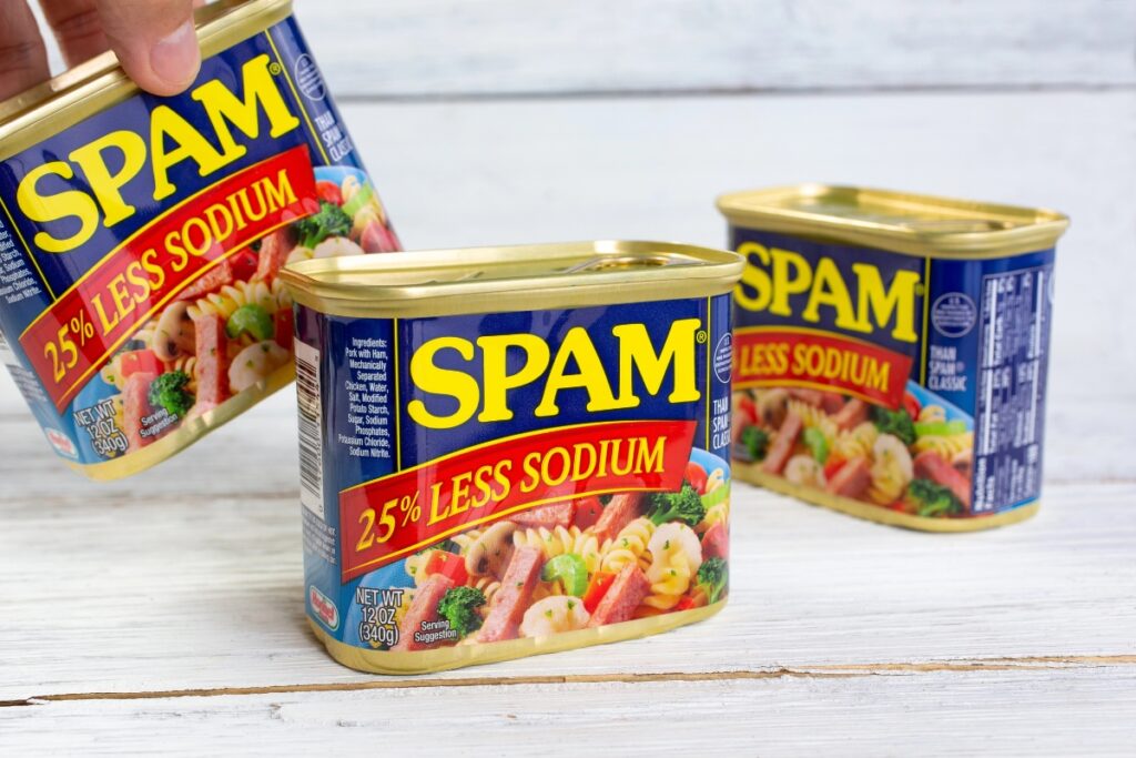 Three cans of Spam placed on a wooden table.