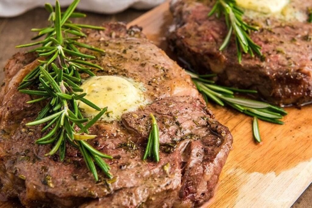 Steak on a wooden board garnished with herbs.