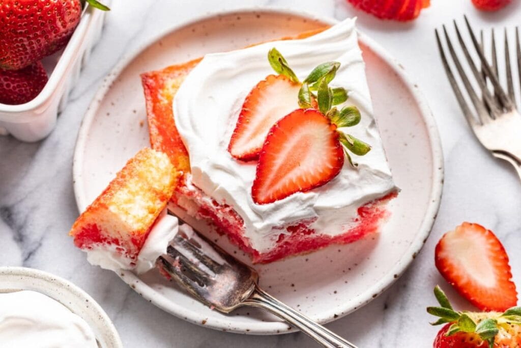Strawberry Jello Poke Cake on a white dessert plate with fork on the side.