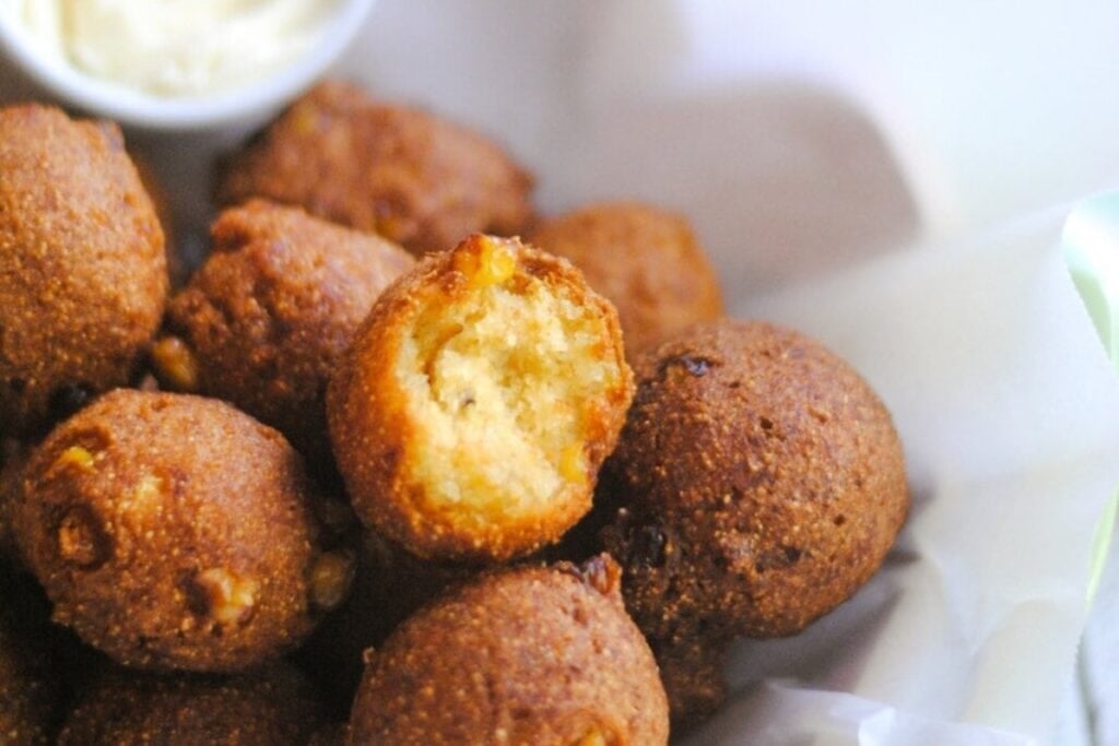 Sweet corn hush puppies on parchment paper with dipping sauce.