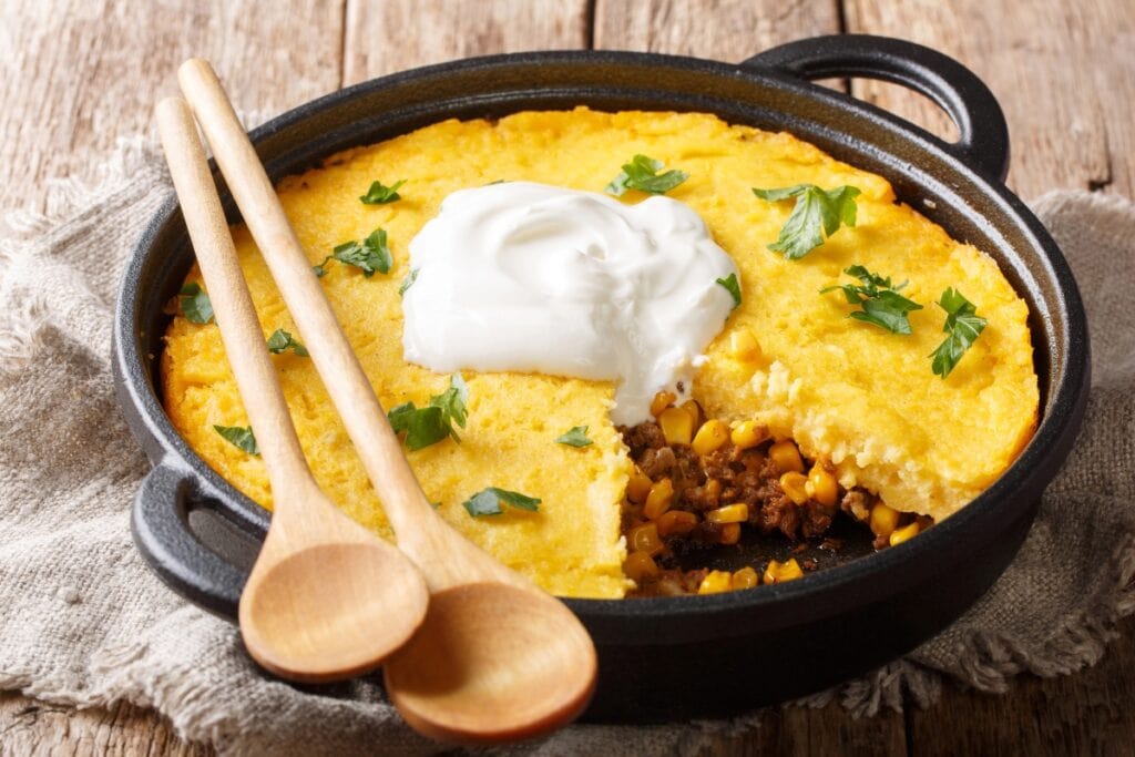 Tamale pie in a black skillet with wooden spoons beside it.