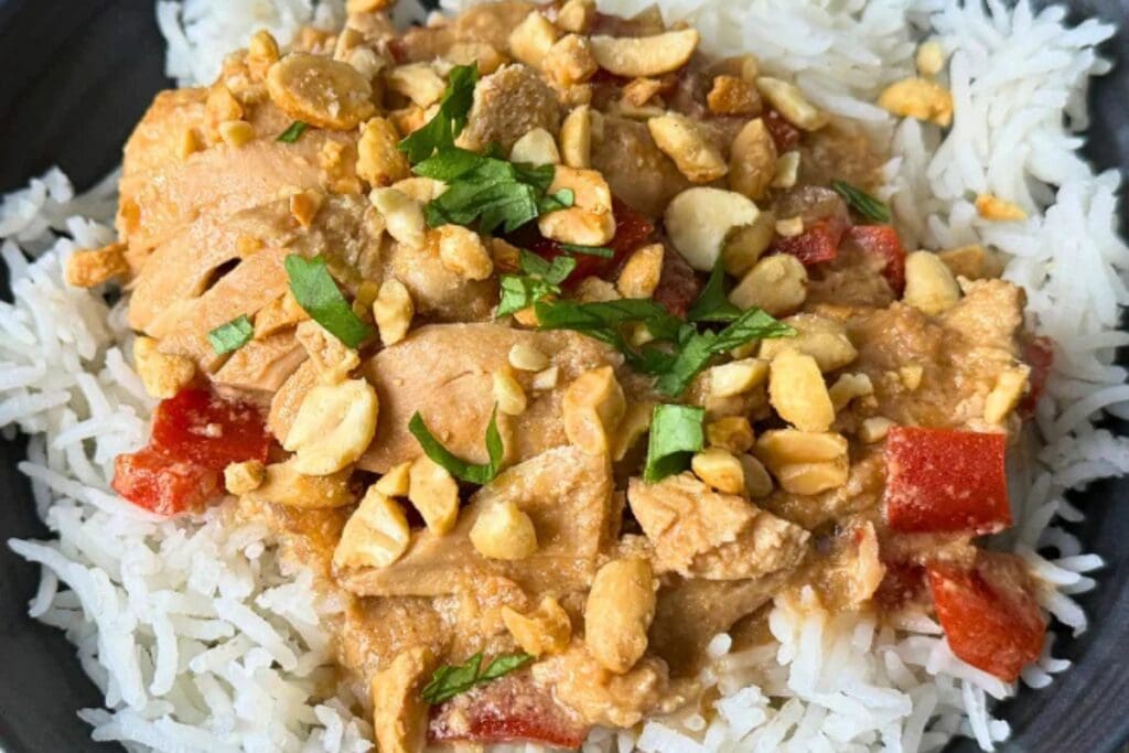 Thai peanut chicken over rice on a black plate.