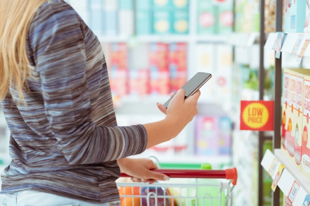 Woman using her phone to compare prices while shopping in a grocery store.