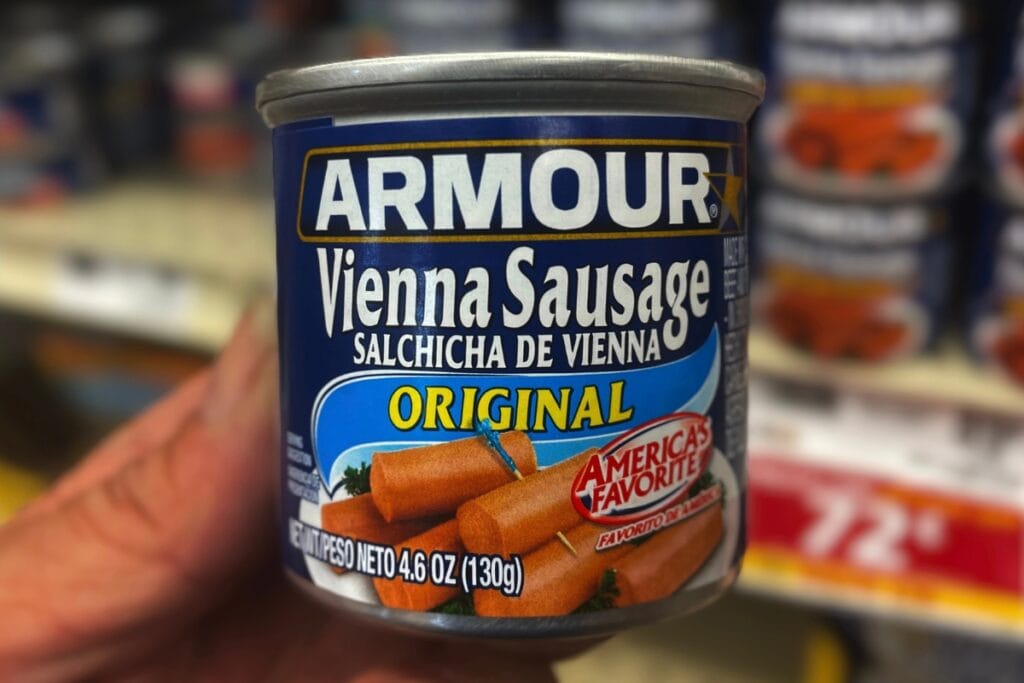 Hand holding a can of Vienna sausages in a grocery store.