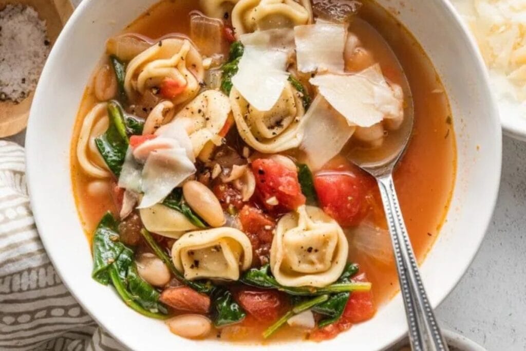 White bean tortellini soup in a white bowl with a spoon.