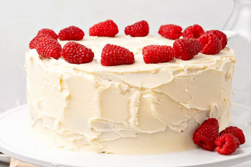 White chocolate raspberry cake placed on a white stand.