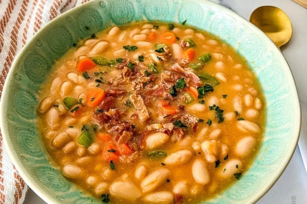 Overhead view of bean soup with carrots and herbs in a green bowl.