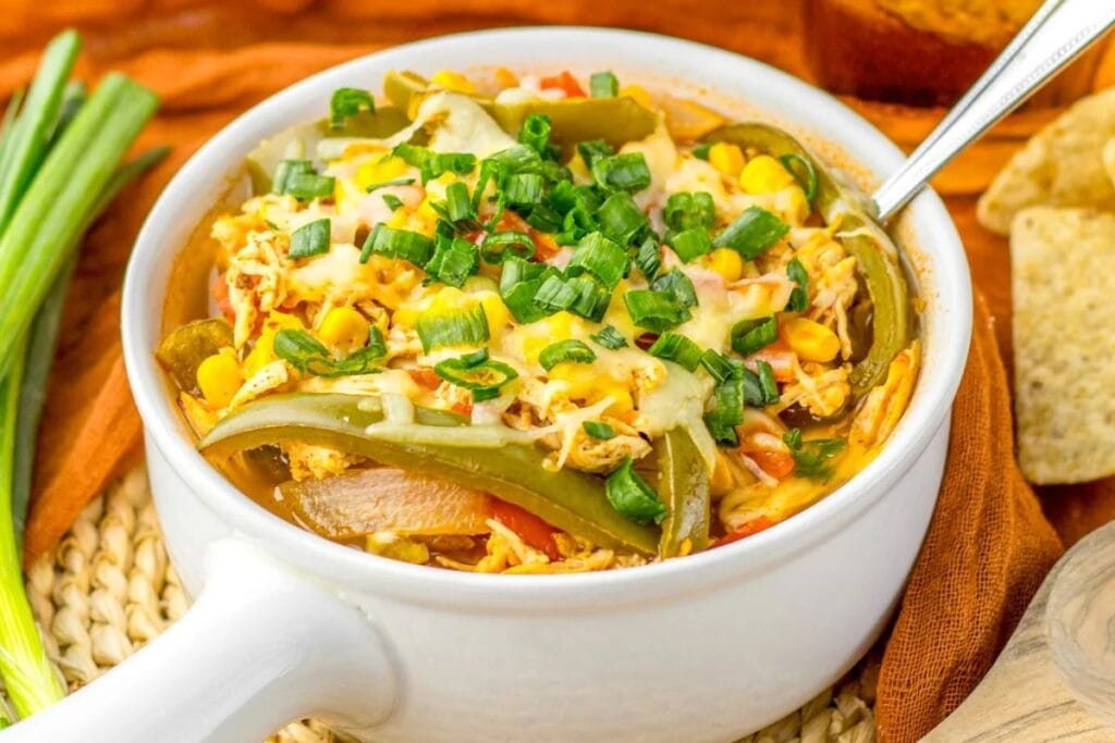 Chicken fajita soup with peppers, corn, cheese, and green onions in a bowl.