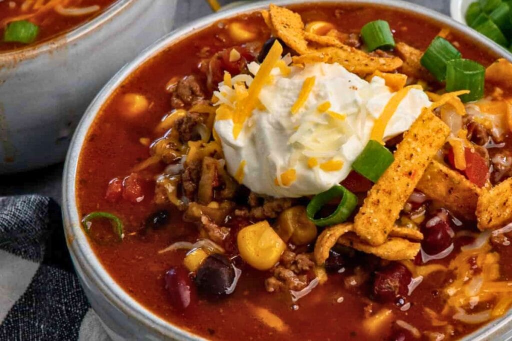 Taco soup with beef, beans, corn, sour cream, cheese, and tortilla strips.