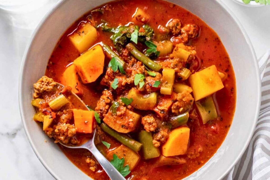 Hamburger soup with potatoes, green beans, and kale in a bowl with spoon.