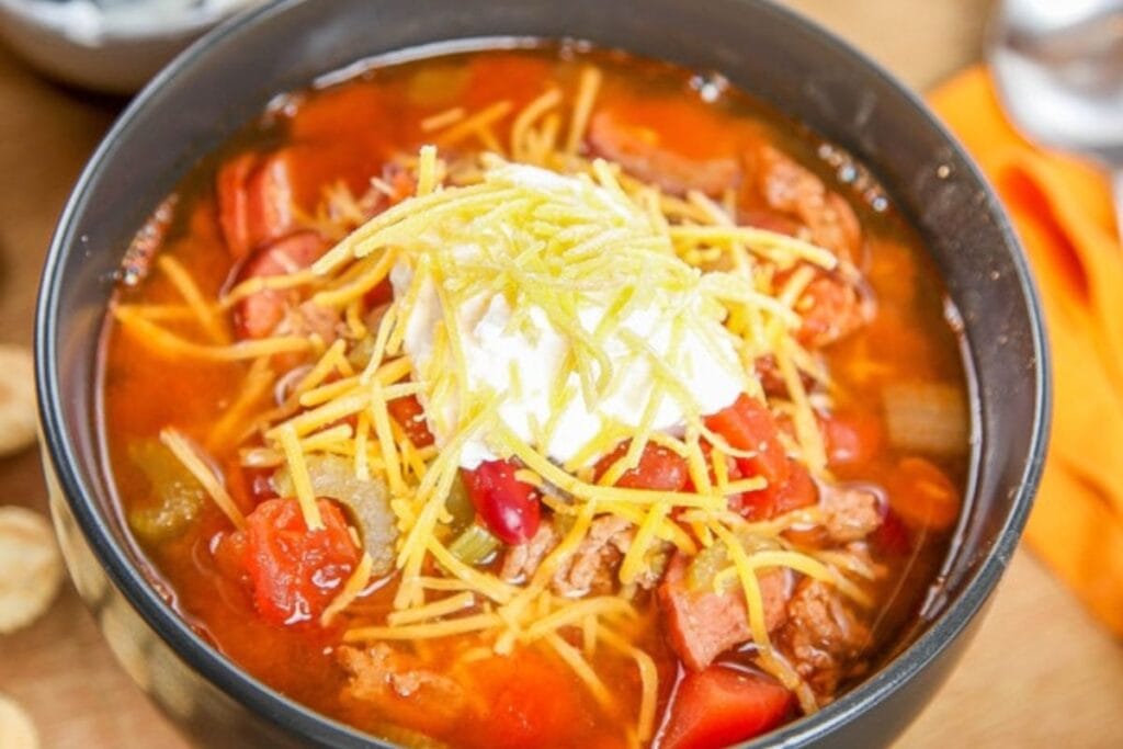Turkey chili in a black bowl, topped with sour cream and shredded cheese.