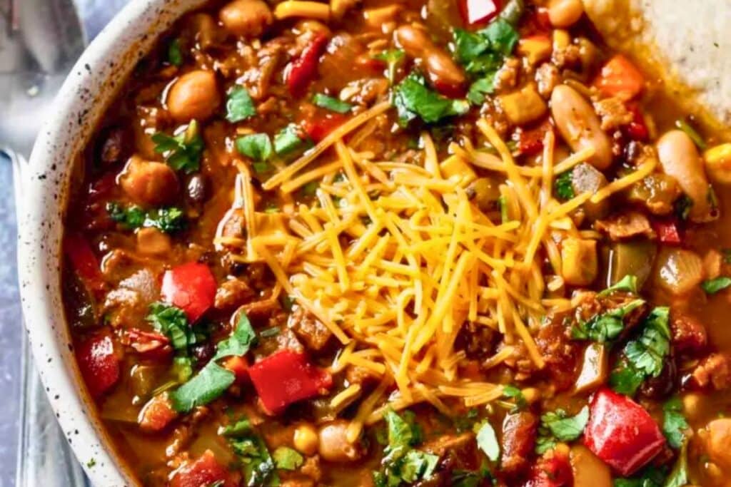 Close-up of vegetarian chili with beans, peppers, and shredded cheese topping.