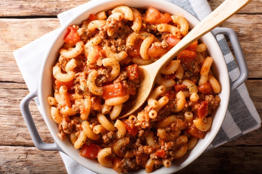 American goulash in a white baking dish with a wooden spoon.