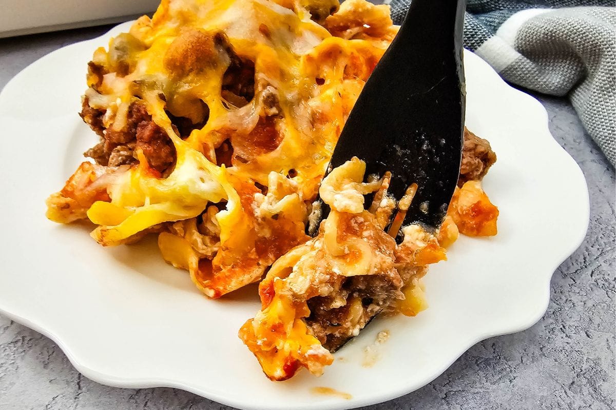 Beef noodle casserole being served with fork on white plate