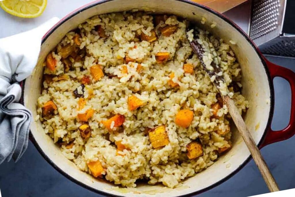 Butternut squash risotto in an oval Dutch oven with a wooden spoon.