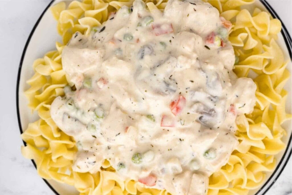Chicken a la king served over pasta on a plate.