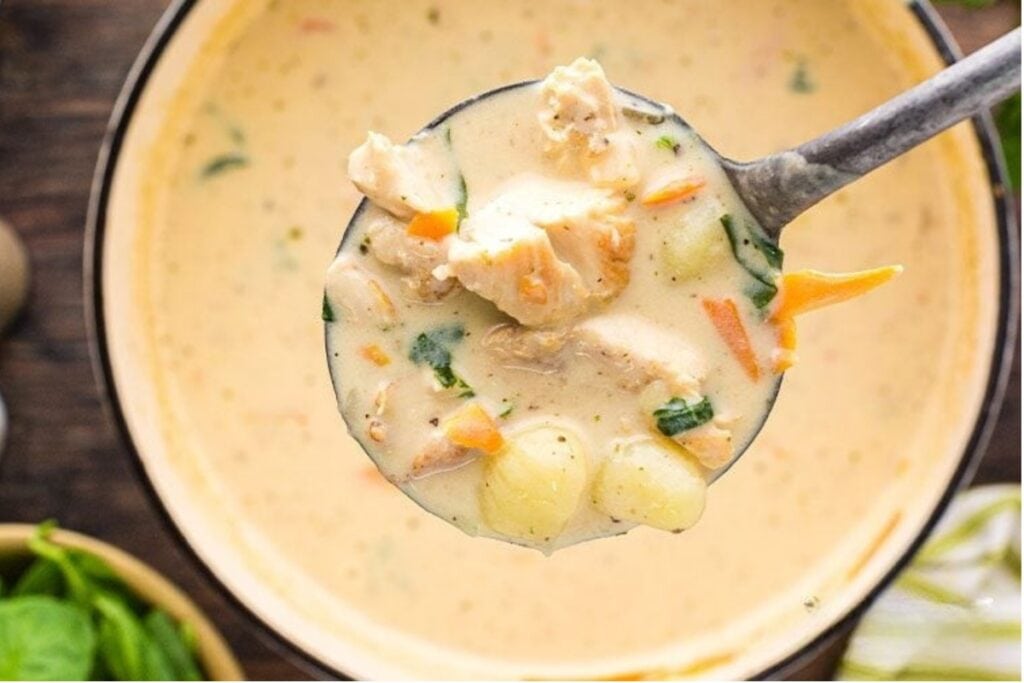 Close-up of chicken and gnocchi soup in a soup ladle.