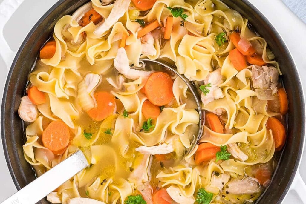 Chicken noodle soup in a pot with a ladle.
