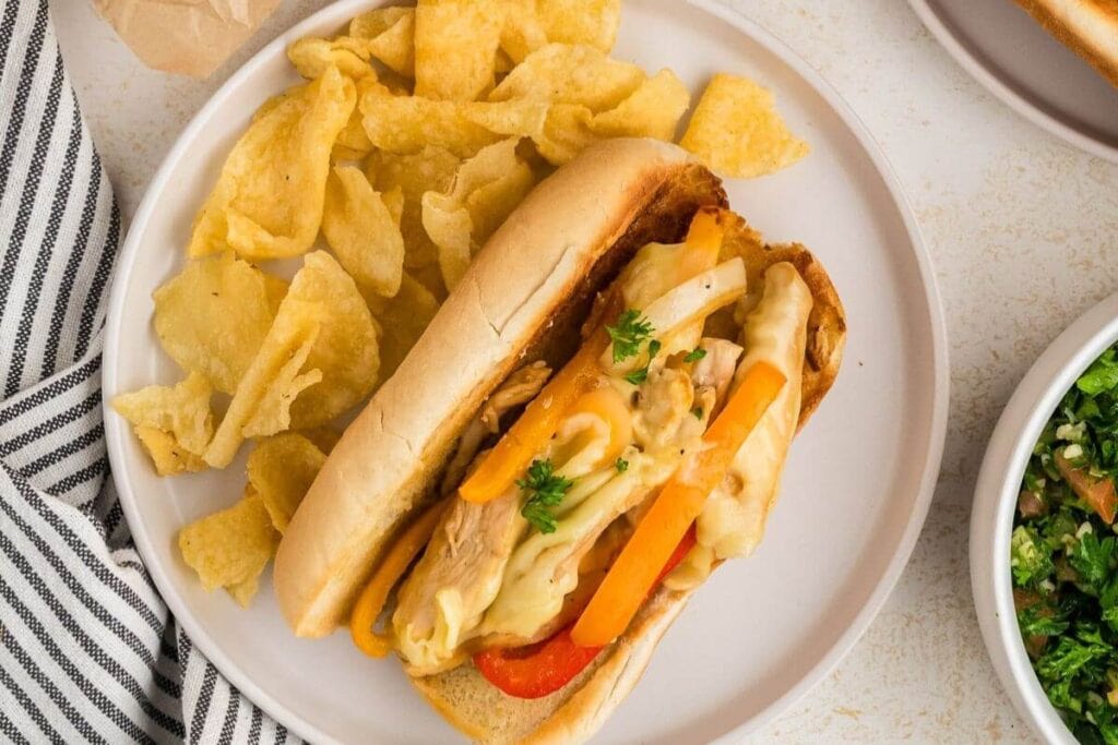 Chicken Philly cheesesteak on a plate served with potato chips.